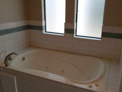 A bath tub sitting under two windows in a bathroom